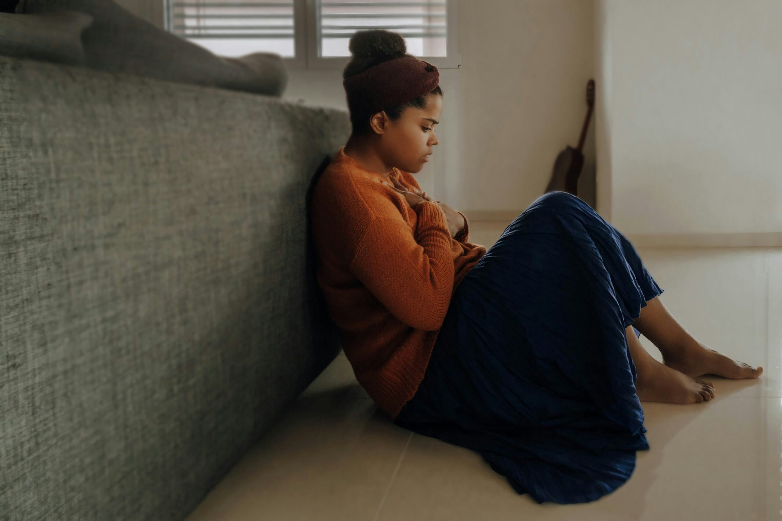 Young woman sitting on the floor with her legs raised and leaning on a gray couch.